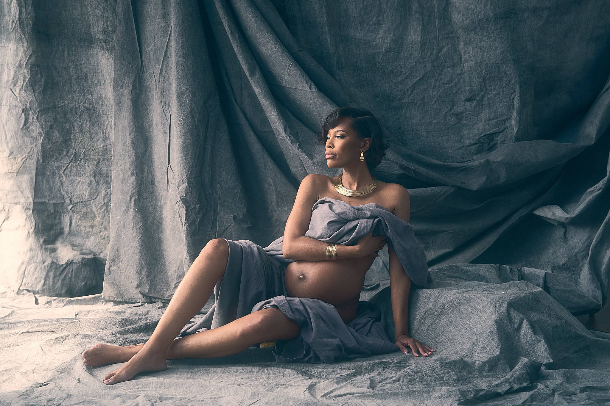 pregnant petite woman sitting on the floor holding her baby bump as she is surrounded by canvas fabric for her orlando florida maternity portrait session